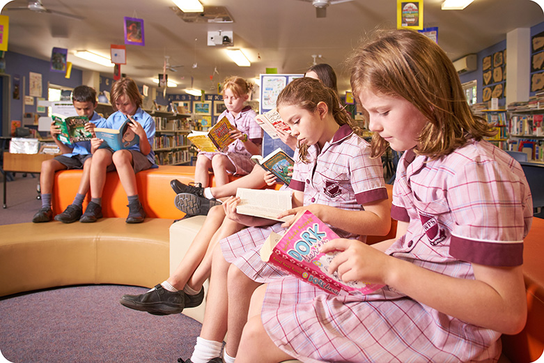 Group of students sitting in a reading area in the school library. They are all reading their books.